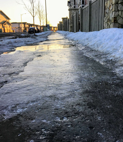 a closeup view of slippery black ice covering a sidewalk