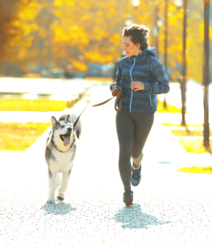 happy young woman jogging with her dog in park